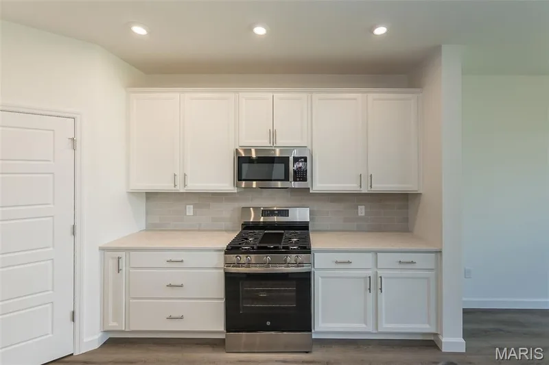 Kitchen with white cabinets, appliances with stainless steel finishes, tasteful backsplash, dark wood-type flooring, and recessed lighting — 717 Southerland Drive, O'Fallon, MO 63368