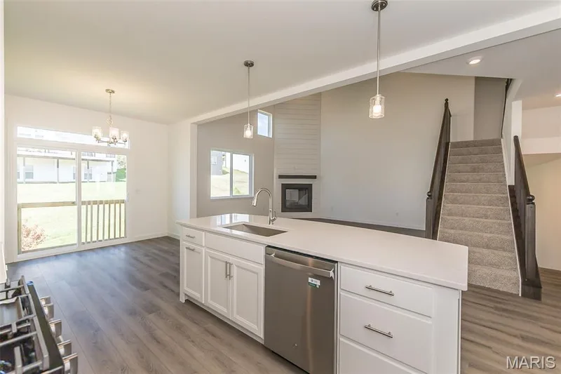 Kitchen with a kitchen island with sink, dishwasher, hanging light fixtures, open floor plan, and light wood-style flooring — 717 Southerland Drive, O'Fallon, MO 63368