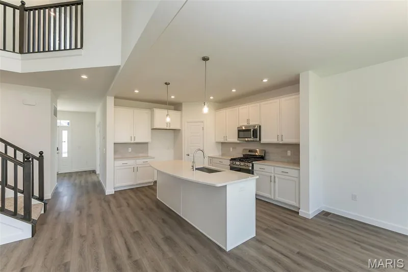 Kitchen with appliances with stainless steel finishes, white cabinetry, an island with sink, hanging light fixtures, and tasteful backsplash — 717 Southerland Drive, O'Fallon, MO 63368