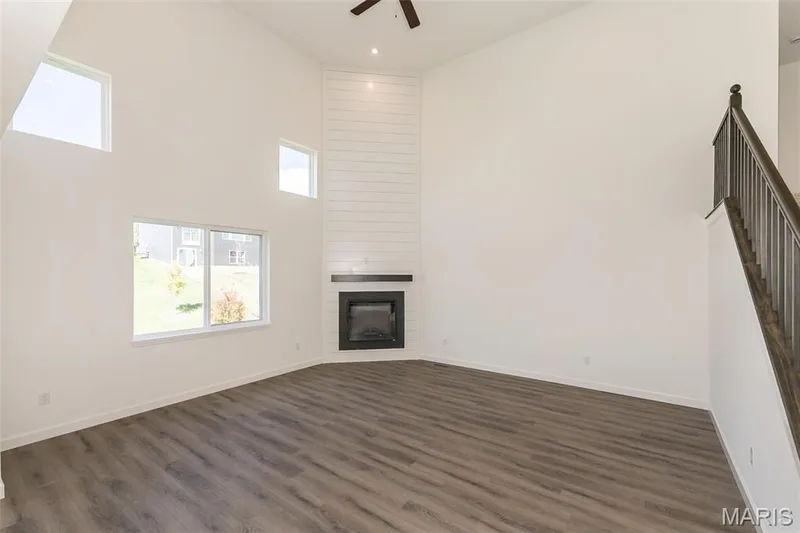 Unfurnished living room featuring a high ceiling, a large fireplace, dark wood finished floors, stairway, and ceiling fan — 717 Southerland Drive, O'Fallon, MO 63368