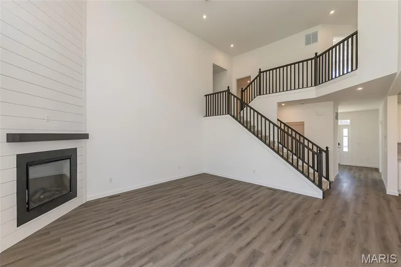 Unfurnished living room featuring stairs, a towering ceiling, dark wood-style flooring, recessed lighting, and a glass covered fireplace — 717 Southerland Drive, O'Fallon, MO 63368