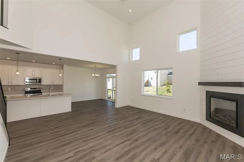 Unfurnished living room with a glass covered fireplace, dark wood-type flooring, recessed lighting, a chandelier, and a high ceiling — 717 Southerland Drive, O'Fallon, MO 63368