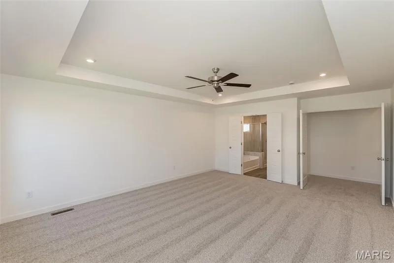 Unfurnished bedroom with a raised ceiling, recessed lighting, a ceiling fan, light colored carpet, and connected bathroom — 717 Southerland Drive, O'Fallon, MO 63368