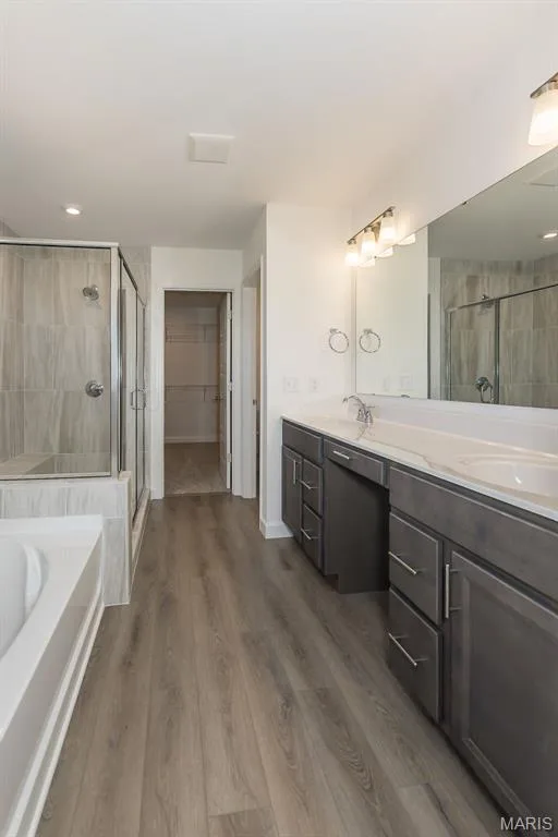 Full bath with a walk in closet, a bath, double vanity, a stall shower, and dark wood-style floors — 717 Southerland Drive, O'Fallon, MO 63368