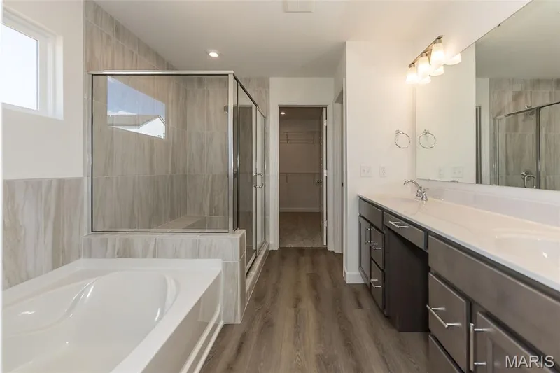 Bathroom with a bath, double vanity, a spacious closet, dark wood finished floors, and a stall shower — 717 Southerland Drive, O'Fallon, MO 63368