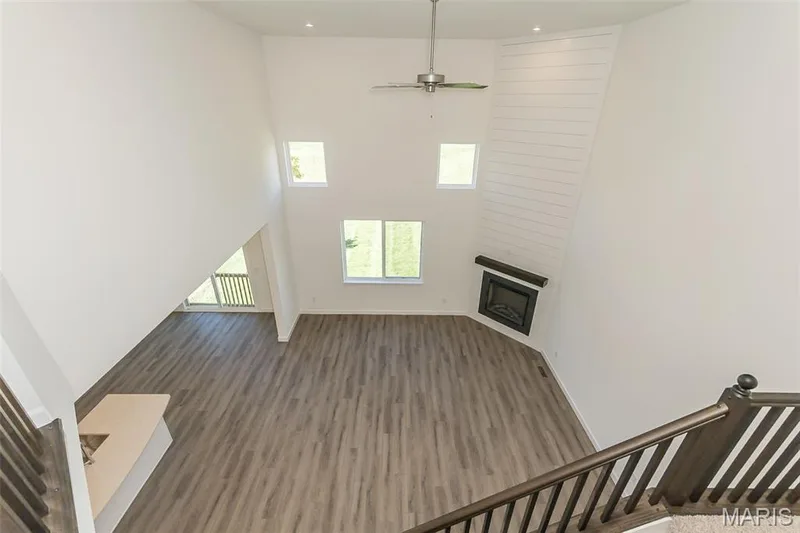 Unfurnished living room with a large fireplace, a high ceiling, a ceiling fan, and dark wood-style flooring — 717 Southerland Drive, O'Fallon, MO 63368