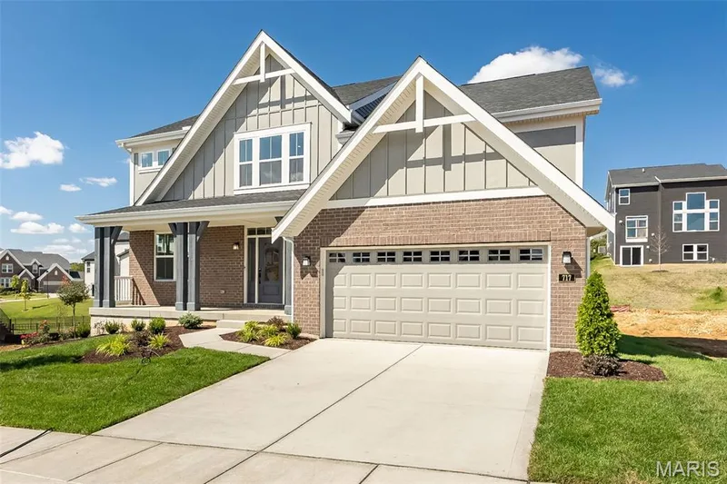 View of front facade with covered porch, board and batten siding, a front yard, driveway, and a garage — 717 Southerland Drive, O'Fallon, MO 63368
